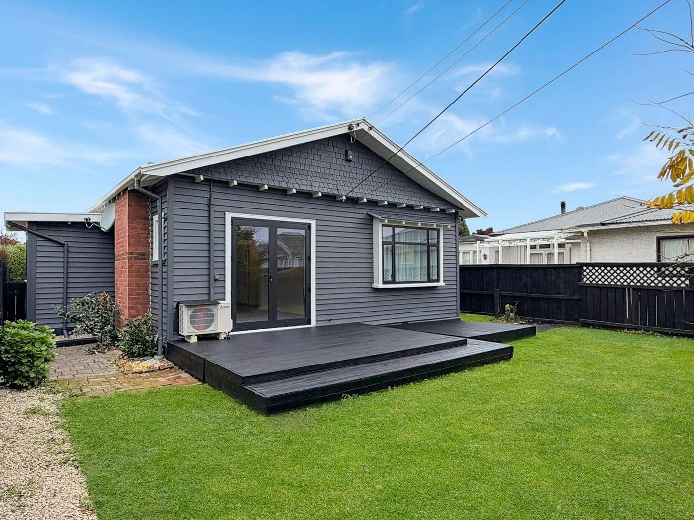 Grey repainted bungalow with a dark timber deck and fresh lawn